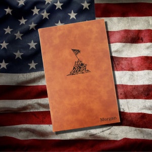 May include: A brown leather journal with a black image of the Iwo Jima flag raising. The journal has the name "Morgan" embossed on the bottom right corner.