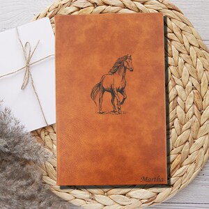May include: A brown leather journal with a horse design and the name "Martha" embossed on the front.