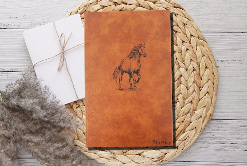 May include: A brown leather journal with a horse design and the name "Martha" embossed on the front.