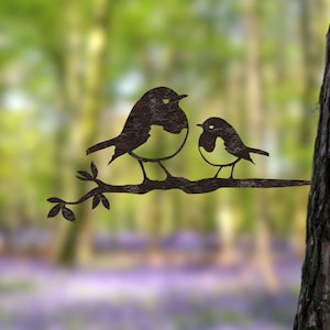 May include: Metal art sculpture of two birds on a branch. The birds are dark with white and black details. The branch has leaves and is set against a blurred forest background. A decorative piece for the garden.