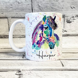 Puede incluir: Taza de cer&aacute;mica blanca con una pintura acuarela colorida de la cabeza de un caballo. La taza tiene un asa blanca y el nombre "Harper" est&aacute; escrito en cursiva negra en la parte inferior.