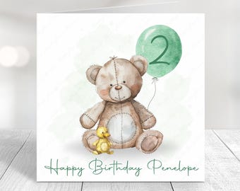 May include: A birthday card featuring a watercolor illustration of a teddy bear holding a green balloon with the number 2. A small yellow duckling sits beside the bear. The card reads "Happy Birthday Penelope" in green script.