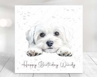 May include: A white birthday card with a cute white dog with brown eyes and paws. The card has a white background with a subtle gray paw print pattern. The text on the card reads "Happy Birthday Wendy".