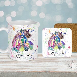 Puede incluir: Un juego de taza y posavasos de cer&aacute;mica blanca con una pintura acuarela colorida de la cabeza de un caballo. La taza y el posavasos est&aacute;n personalizados con el nombre "Emma" en escritura negra.