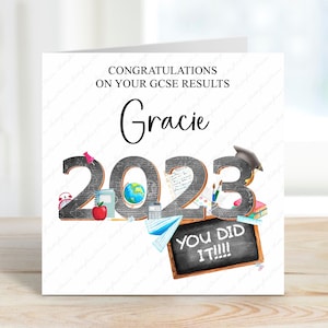 May include: A white card with a black and white illustration of school supplies and the year 2023. The text "Congratulations on your GCSE results Gracie" is at the top of the card. The text "You did it!!!" is on a chalkboard at the bottom of the card.
