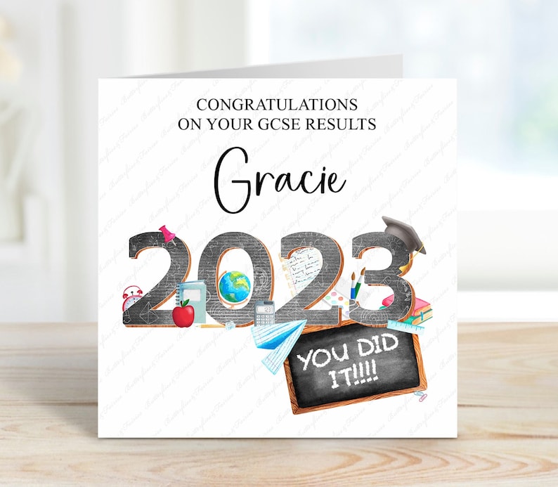 May include: A white card with a black and white illustration of school supplies and the year 2023. The text "Congratulations on your GCSE results Gracie" is at the top of the card. The text "You did it!!!" is on a chalkboard at the bottom of the card.