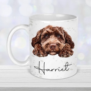Peut inclure: Une tasse en céramique blanche avec une illustration d'un chien brun et noir. Le chien regarde la caméra avec ses pattes reposant sur le bord de la tasse. Le texte "Harriet" est imprimé sur la tasse.