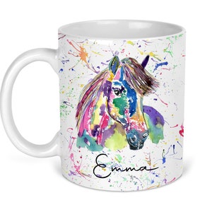 Puede incluir: Taza de cer&aacute;mica blanca con una pintura de acuarela colorida de la cabeza de un caballo. El fondo es blanco con salpicaduras de pintura de colores. El nombre "Emma" est&aacute; escrito en cursiva en la parte inferior de la taza.