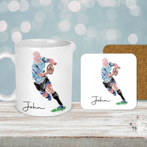 May include: White ceramic mug with a watercolor illustration of a rugby player running with the ball. The mug has the name "John" written on it.