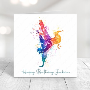 May include: A white greeting card with a watercolor illustration of a breakdancer in a handstand. The dancer is depicted in vibrant colors including blue, purple, orange, and green. The words "Happy Birthday Jackson" are written in teal script.