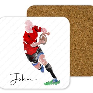 May include: A square coaster with a watercolor illustration of a rugby player in a red jersey, black shorts, and blue socks, holding a brown ball. The name "John" is written in cursive. A second cork coaster is visible.