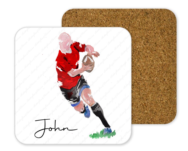May include: A square coaster with a watercolor illustration of a rugby player in a red jersey, black shorts, and blue socks, holding a brown ball. The name "John" is written in cursive. A second cork coaster is visible.