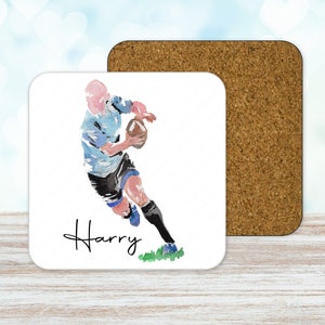 May include: A white square coaster with a watercolor illustration of a rugby player running with the ball. The player is wearing a blue and white jersey, black shorts, and black socks. The name "Harry" is written in cursive below the player.