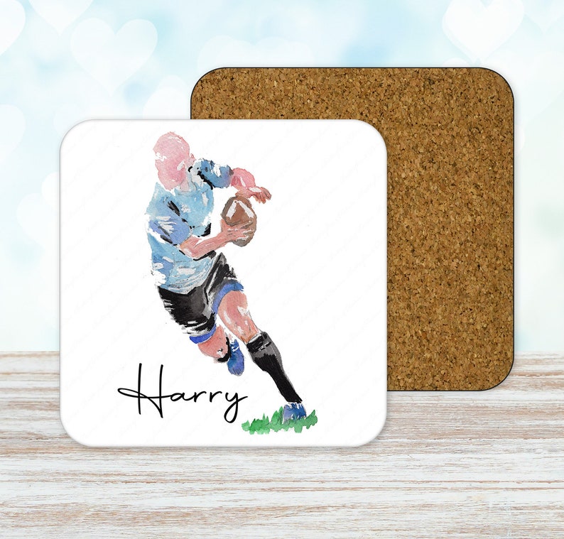 May include: A white square coaster with a watercolor illustration of a rugby player running with the ball. The player is wearing a blue and white jersey, black shorts, and black socks. The name "Harry" is written in cursive below the player.