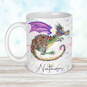 May include: White ceramic mug with a vibrant watercolour dragon design. The dragon has purple wings and is surrounded by colourful paint splatters. The name "Nathan" is written on the mug in a script font.
