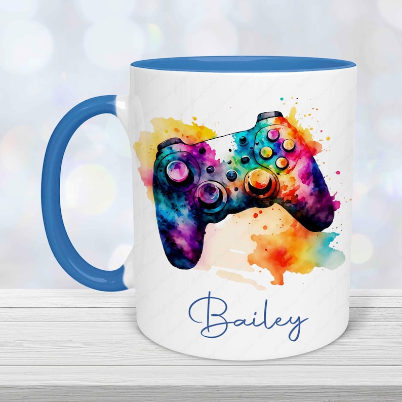 Personalised gamer mug with colourful watercolour gaming controller design and custom name printed underneath.  Mug has a blue handle and is blue inside.