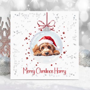 May include: A square Christmas greeting card featuring a central illustration of a brown puppy wearing a red and white Santa hat inside a clear glass ornament. The text Merry Christmas Harry is printed in red below the ornament graphic.