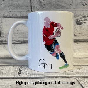 May include: White ceramic mug with a colorful illustration of a person playing rugby. The mug has a handle and the name "Guy" is written in cursive on the bottom.