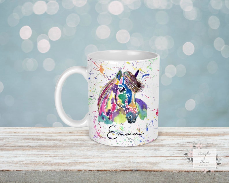 Puede incluir: Taza de cer&aacute;mica blanca con una pintura de acuarela colorida de la cabeza de un caballo. La taza tiene un asa y el nombre "Emma" est&aacute; escrito en la parte inferior del dise&ntilde;o.