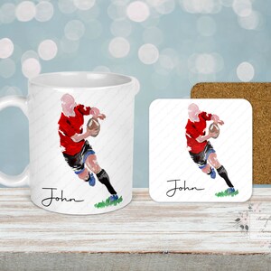 May include: A white ceramic mug and square coaster set featuring a watercolor illustration of a rugby player in a red jersey. The player is running with a football. The name "John" is written in cursive. A cork coaster is also included.