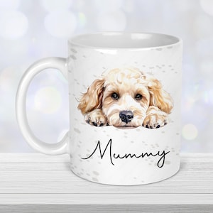 May include: White ceramic mug with a watercolour illustration of a golden doodle puppy. The puppy is lying down. The word "Mummy" is written in a cursive font on the mug. The mug has a white handle.
