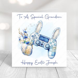 May include: Easter greeting card with a blue and white watercolor design. The card features a video game controller with bunny ears, blue flowers, and decorated Easter eggs. Text reads "To A Special Grandson" and "Happy Easter Joseph."