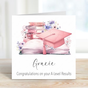 May include: A pink graduation cap sits on top of a stack of books with pink and purple flowers. The text "Gracie" and "Congratulations on your A-Level Results" are printed below the image.