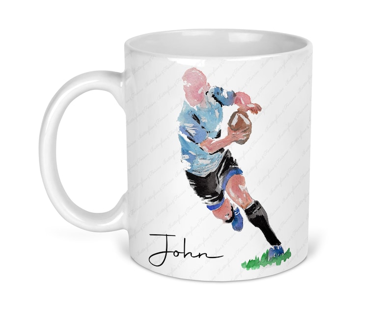 May include: White ceramic mug with a watercolor illustration of a rugby player running with the ball. The player is wearing a blue and white jersey and black shorts. The mug has the name "John" written in black cursive at the bottom.
