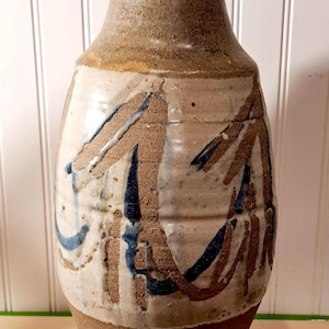 May include: A ceramic vase with a brown, white, and blue glaze. The vase has a wide base and a narrow neck. It is decorated with abstract designs.