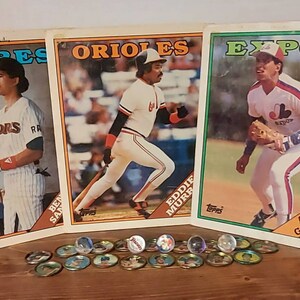 May include: Three baseball cards featuring players from the Padres, Orioles, and Expos teams. The cards are in mint condition and feature the Topps logo. The cards are surrounded by a collection of small, round, glass marbles.