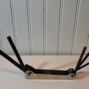 May include: A multi-tool hex key set with black hex keys and a silver metal base. The keys are arranged in an open fan shape, showing different sizes. The tool is designed for tightening or loosening bolts and screws.