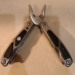 May include: Silver multi-tool pliers with black rubberized handles. The pliers have a Max Tools logo on the handle.