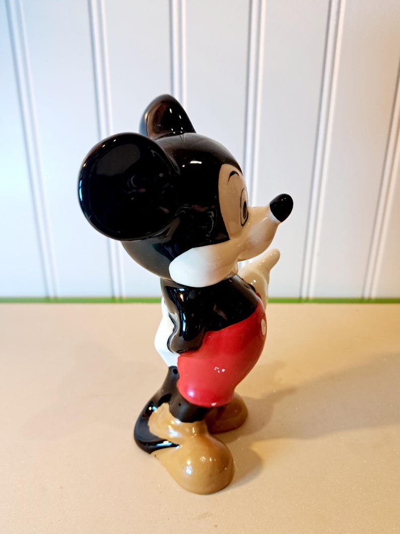May include: A black and white ceramic figurine of Mickey Mouse wearing red shorts and brown shoes. The figurine is standing with its right arm raised.