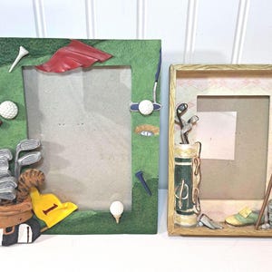 May include: Two decorative picture frames with golf-themed embellishments. One frame is green with golf clubs, a golf ball, and a red flag. The other frame is tan with a golf bag, golf clubs, and a red flag.