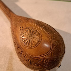 May include: A wooden musical instrument with intricate carvings. The instrument is shaped like a gourd and has a round, carved design in the center.