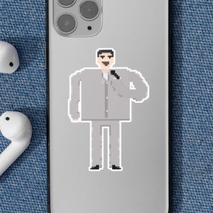 May include: A silver phone case with a pixelated image of a person wearing a gray suit and holding a microphone. Two white wireless earbuds are on a blue denim background.