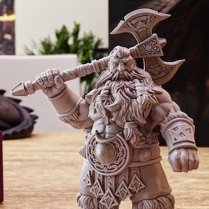 Könnte beinhalten: Eine detaillierte Miniaturfigur eines Zwergenkriegers, der eine große Axt hält und einen gehörnten Helm, eine Kettenrüstung und einen pelzgefütterten Umhang trägt. Die Figur ist in Grautönen und Braun bemalt.