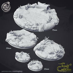 Puede incluir: Cuatro bases redondas de diferentes tamaños, impresas en 3D en gris, con un tema de bosque. Las bases presentan un arroyo, rocas y hierba. Las bases tienen un diámetro de 25 mm, 50 mm, 75 mm y 100 mm.