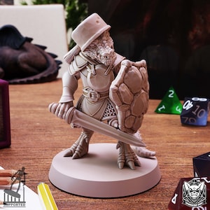 Puede incluir: Una figura miniatura de una criatura parecida a un lagarto que lleva un casco y una armadura, sosteniendo una espada y un escudo. La figura está pintada de color marrón claro y está de pie sobre una base redonda.