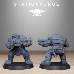 May include: Two gray miniature figures of heavily armored soldiers, each holding a large gun. The figures are on black bases. The word "STATIONFORGE" is above the figures, along with a skull and wings logo.