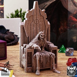 Puede incluir: Miniatura beige de un esqueleto sentado en un trono gótico ornamentado. El esqueleto lleva una corona y ropa desgarrada. Dados y un logotipo son visibles en el fondo.