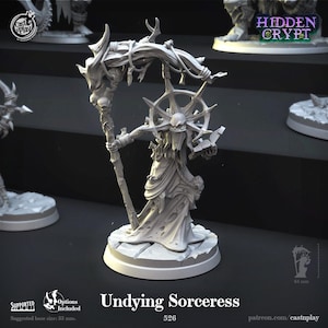 Op de afbeelding: Een grijze hars miniatuurfiguur getiteld Undying Sorceress 526, met een figuur met capuchon en een halo met stekels, die een open boek en een grote, gedraaide staf vasthoudt. Het figuur staat op een ronde basis met een aanbevolen maat van 35 mm.