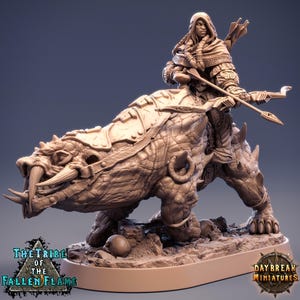 May include: A detailed miniature figurine of a warrior riding a reptilian beast. The warrior is armed with a bow and arrows. The base of the figurine has the text "THE TRIBE OF THE FALLEN FLAME" and "DAYBREAK MINIATURES". The color is a light brown.