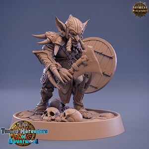 May include: A detailed figurine of a goblin warrior, holding an axe and shield. The goblin is adorned with armor and large tusks. The base features skulls and the text "The Tusked Marauders of Gauntwood."