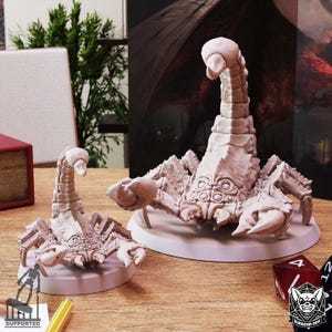 Può includere: Due figurine di scorpione di colore chiaro, una grande e una piccola, sono esposte su una superficie di legno. Gli scorpioni hanno esoscheletri dettagliati e sono posati con i loro pungiglioni sollevati. Le figurine sono probabilmente per giochi da tavolo o esposizioni.