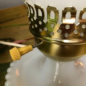 May include: Close-up of a white glass lamp base with a gold metal trim and a white cord with a yellow switch.