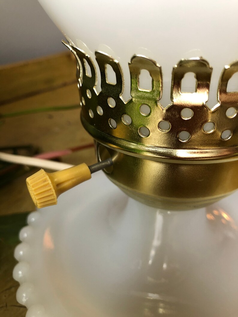 May include: Close-up of a white glass lamp base with a gold metal trim and a white cord with a yellow switch.