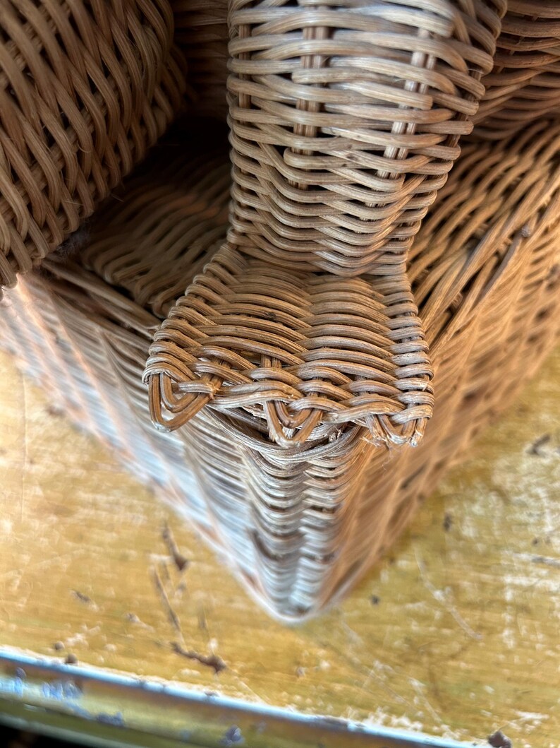 May include: Close-up of a woven wicker basket with a rounded corner. The basket is made of light brown wicker and has a textured surface. The basket appears to be sturdy and well-crafted.