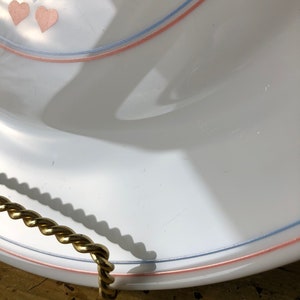 May include: White ceramic serving tray with a pink and blue trim and a gold rope handle. The tray has a heart design with pink and blue hearts.