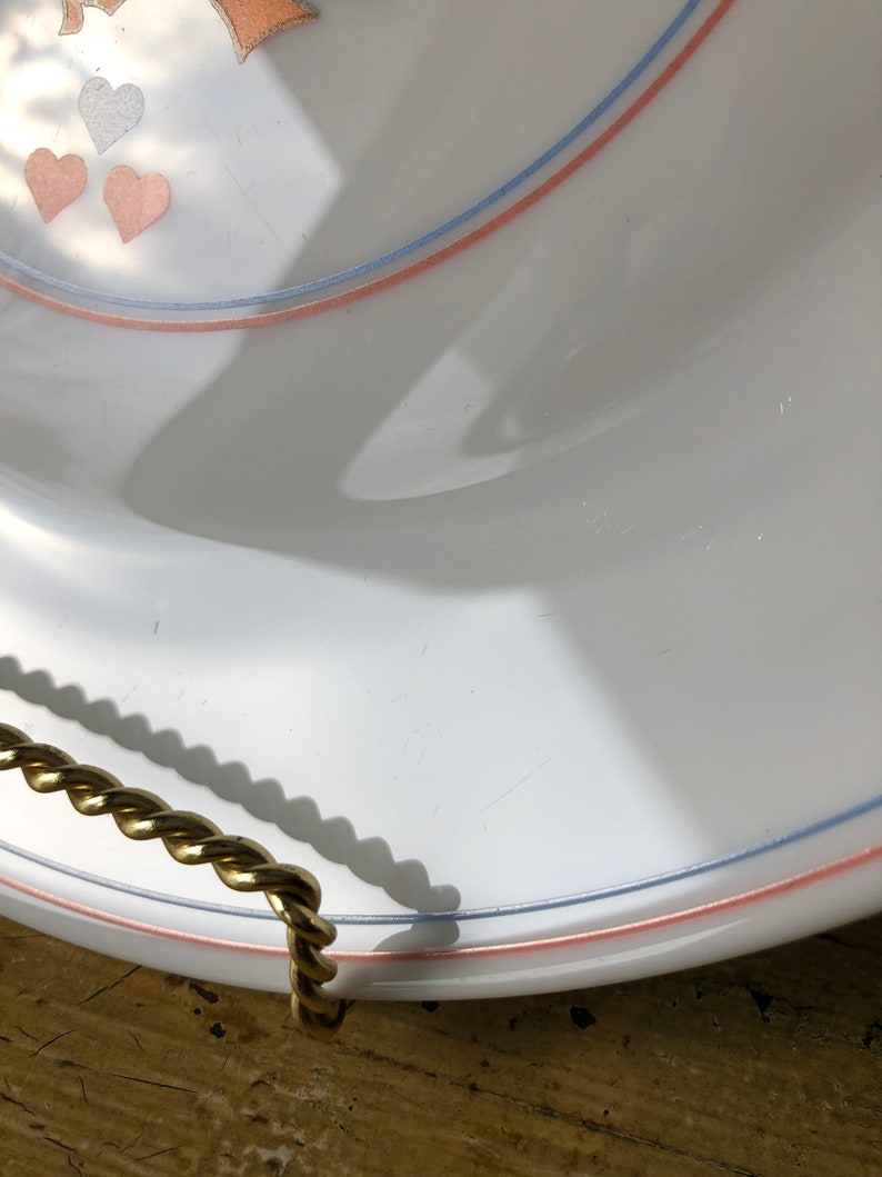 May include: White ceramic serving tray with a pink and blue trim and a gold rope handle. The tray has a heart design with pink and blue hearts.